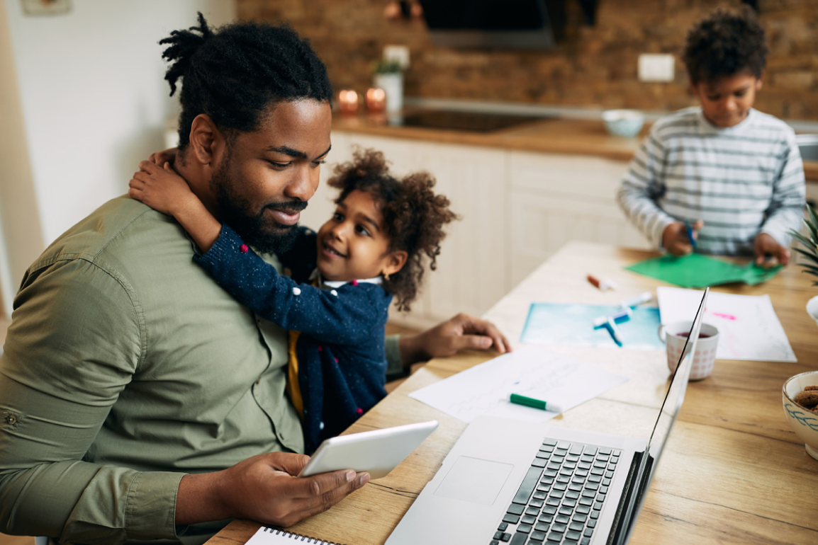 Student studies at the kitchen table as his young kids play in the area.  