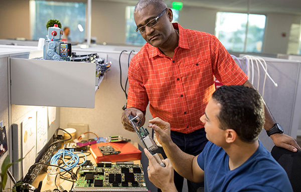 A systems security officer works with a team member, checking computer equipment