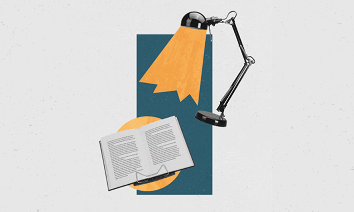 Lamp shining down on an open book in the center of the frame.